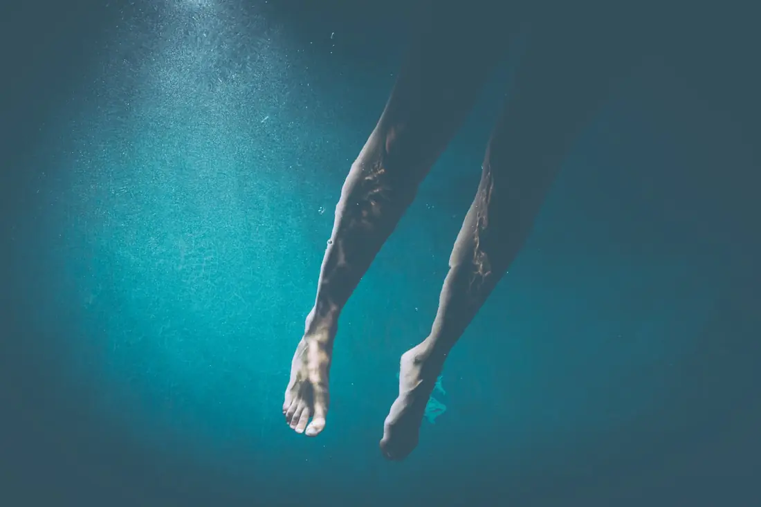 Legs of a person swimming underwater in a blue pool